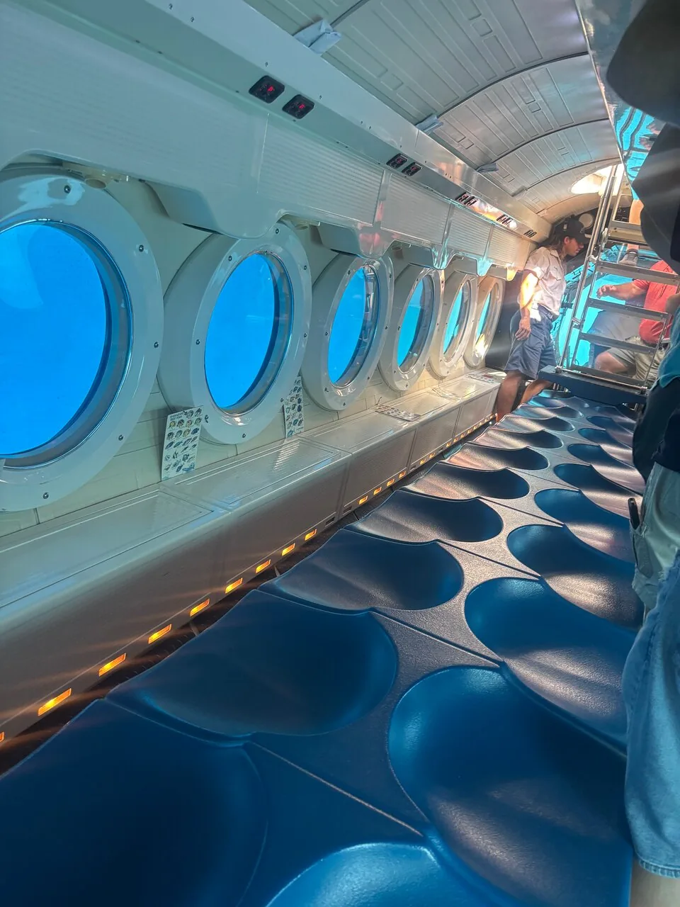 Gästefoto der U-Boot-Kabine mit einer Reihe runder Bullaugen und blauen Sitzen
