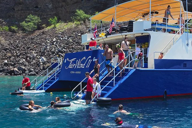Snorkellers with floats in clear water beside the stern of a large blue catamaran