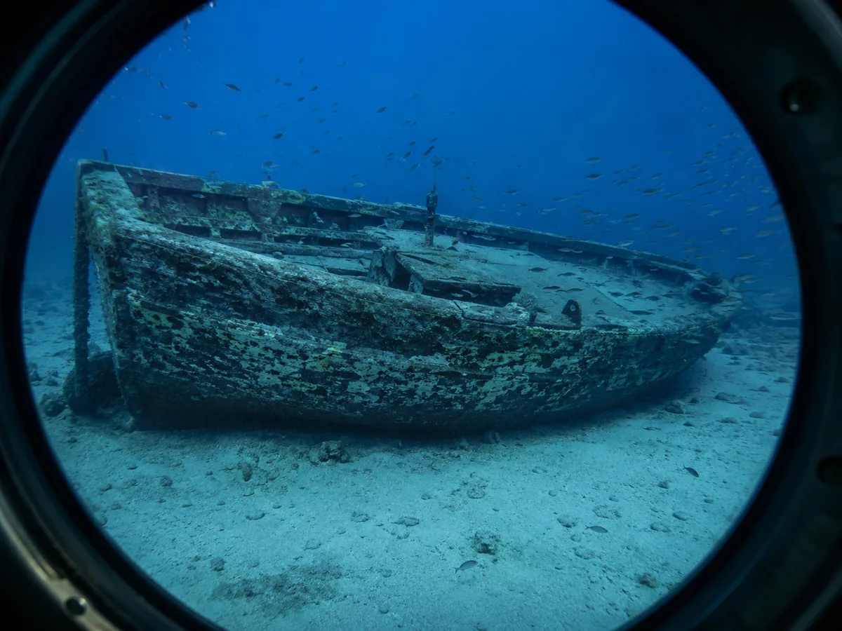Ein kleines gesunkenes Holzboot auf weißem Sand, gesehen durch ein rundes U-Boot-Bullauge